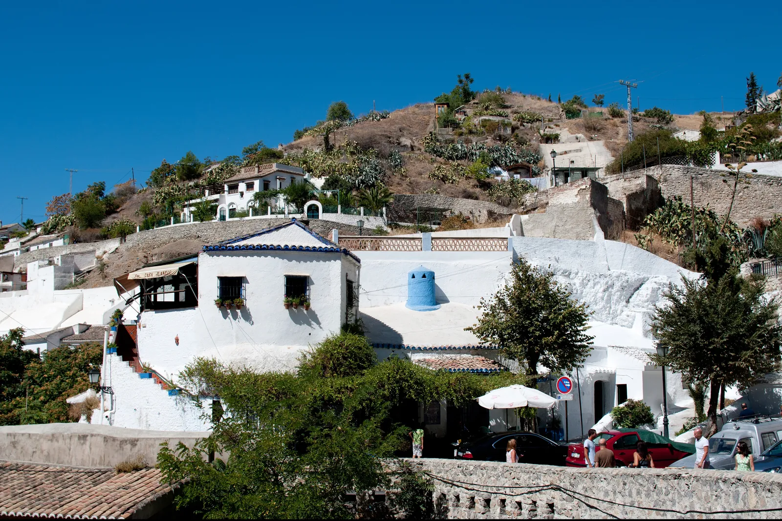 Whitewashed houses and cave dwellings stepping up the Sacromonte hillside beneath clear sky; a general view of the quarter