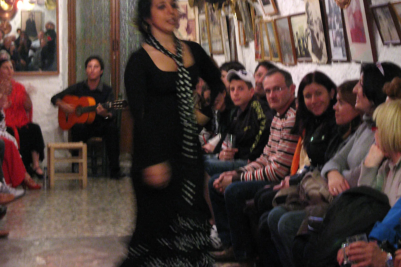 A dancer in black with a polka-dot scarf passes a seated guitarist as spectators watch from the cave's side benches; April 2009, labelled on Wikimedia Commons as Cueva de la Rocío